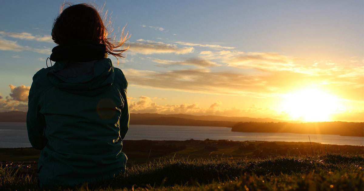 Frau am Feld mit untergehender Sonne im Hintergrund